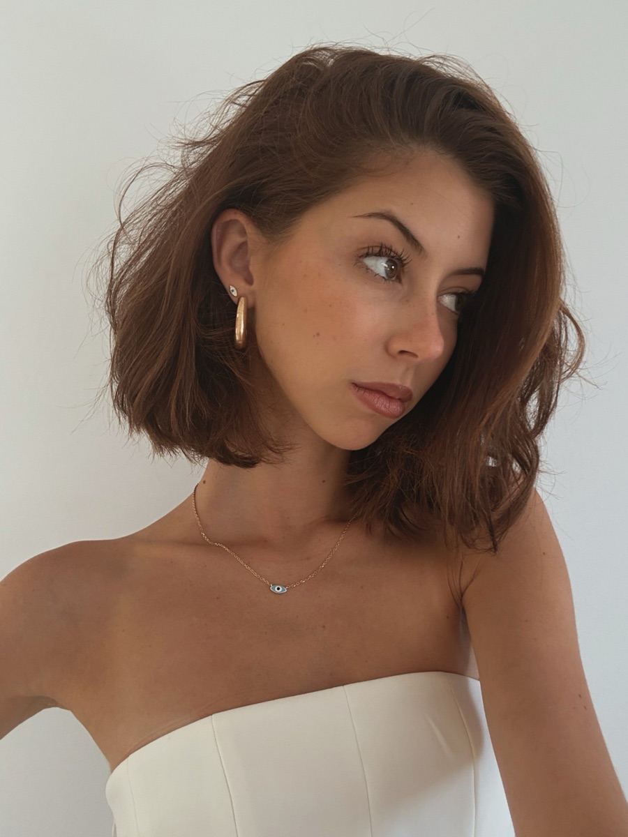 Lucia Mae Dias in a white strapless top, looking over her shoulder